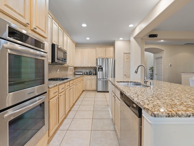 kitchen with light brown cabinetry, appliances with stainless steel finishes, a sink, and decorative backsplash