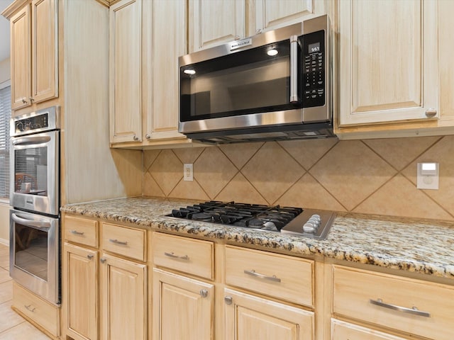 kitchen with appliances with stainless steel finishes, light brown cabinets, light stone counters, and tasteful backsplash