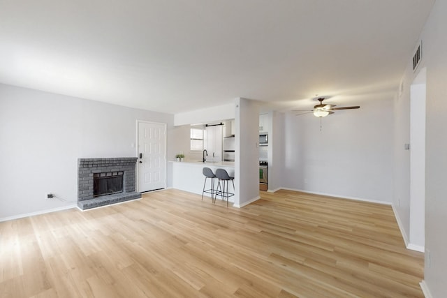 unfurnished living room with ceiling fan, a sink, baseboards, light wood-type flooring, and a brick fireplace