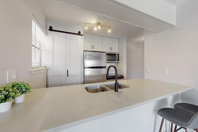 kitchen featuring a barn door, appliances with stainless steel finishes, a breakfast bar, a peninsula, and a sink