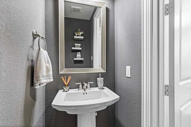 bathroom featuring visible vents, a textured wall, and a sink