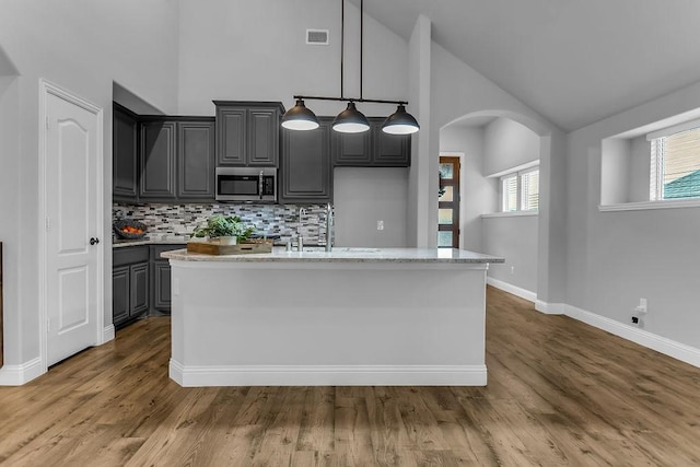 kitchen with stainless steel microwave, dark wood-style floors, visible vents, and arched walkways