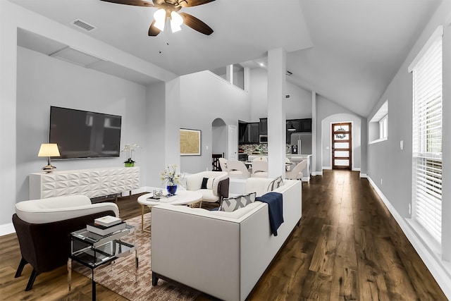 living room with visible vents, high vaulted ceiling, dark wood finished floors, arched walkways, and baseboards