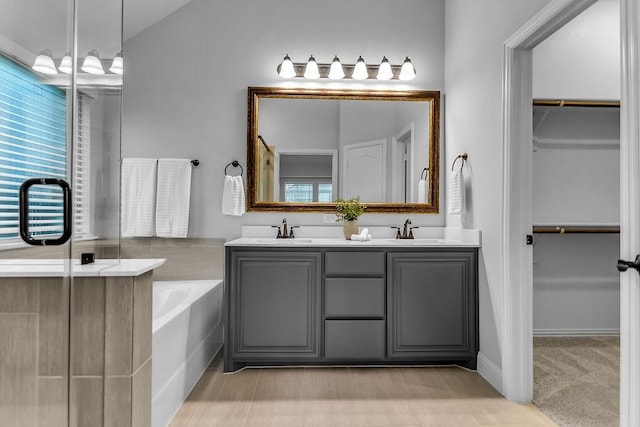 bathroom with a garden tub, a spacious closet, double vanity, and a sink