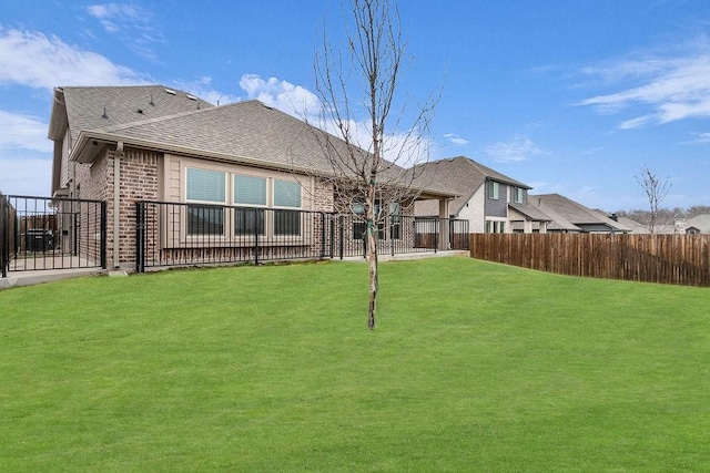 rear view of property with brick siding, a lawn, roof with shingles, and fence