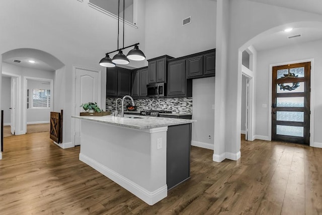 kitchen featuring visible vents, a sink, stainless steel microwave, arched walkways, and dark wood-style flooring