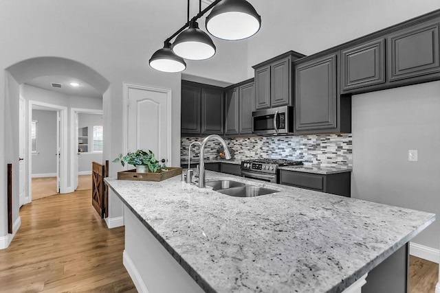 kitchen with a sink, backsplash, arched walkways, appliances with stainless steel finishes, and light stone countertops