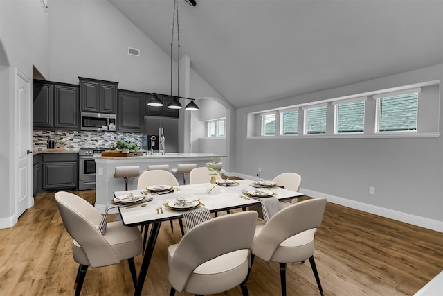 dining space with arched walkways, visible vents, light wood-style flooring, and baseboards