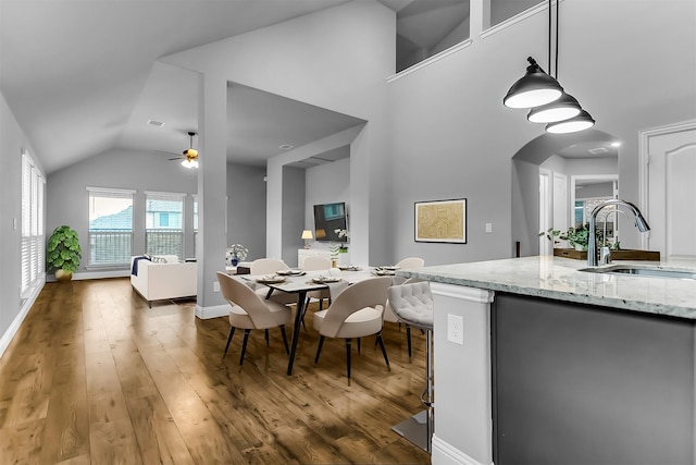 dining room with a ceiling fan, baseboards, lofted ceiling, arched walkways, and wood-type flooring