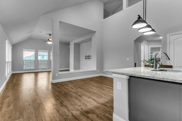 kitchen featuring light stone counters, wood finished floors, ceiling fan, a sink, and vaulted ceiling