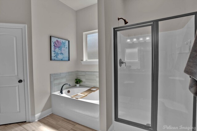 bathroom featuring wood finished floors, a shower stall, a bath, and baseboards