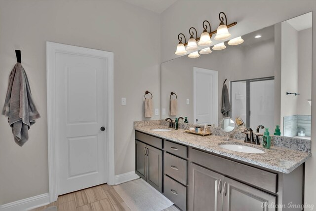 bathroom with double vanity, a shower stall, baseboards, and a sink