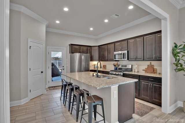 kitchen featuring a breakfast bar area, appliances with stainless steel finishes, a kitchen island with sink, dark brown cabinetry, and a sink