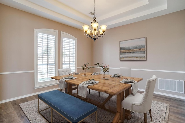 dining area with a tray ceiling, visible vents, a notable chandelier, and wood finished floors