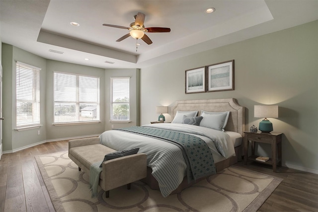 bedroom with a tray ceiling, wood finished floors, visible vents, and baseboards