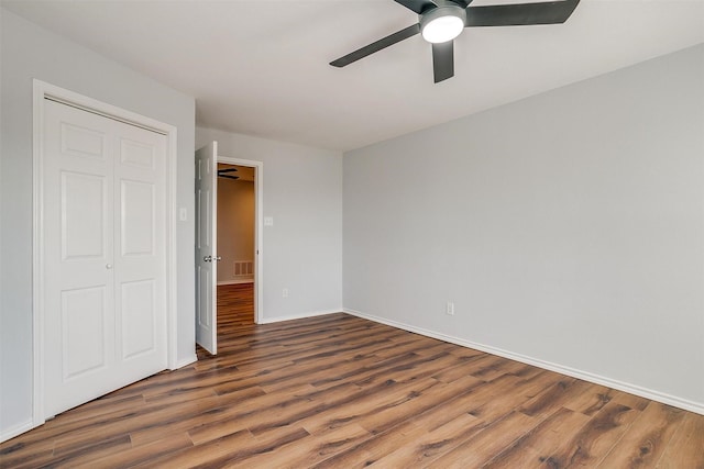 unfurnished bedroom with a closet, visible vents, a ceiling fan, wood finished floors, and baseboards