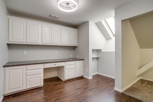 unfurnished office with a skylight, visible vents, baseboards, built in study area, and dark wood-style floors