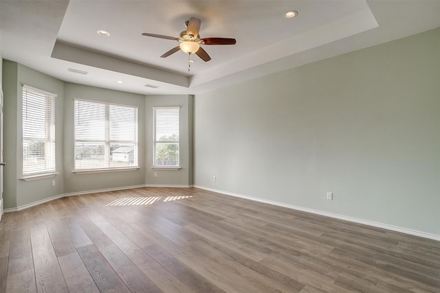 unfurnished room with ceiling fan, wood finished floors, visible vents, baseboards, and a tray ceiling