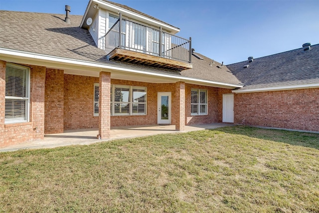 rear view of house featuring roof with shingles, a yard, brick siding, a patio, and a balcony