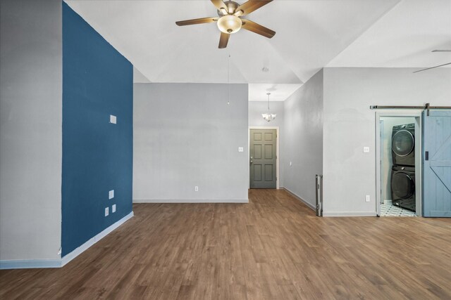 empty room with a barn door, stacked washer / dryer, ceiling fan, wood finished floors, and baseboards