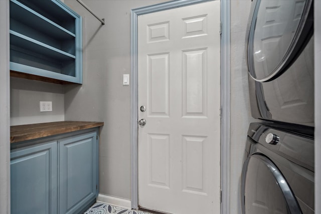 laundry area featuring stacked washer / dryer, cabinet space, and baseboards