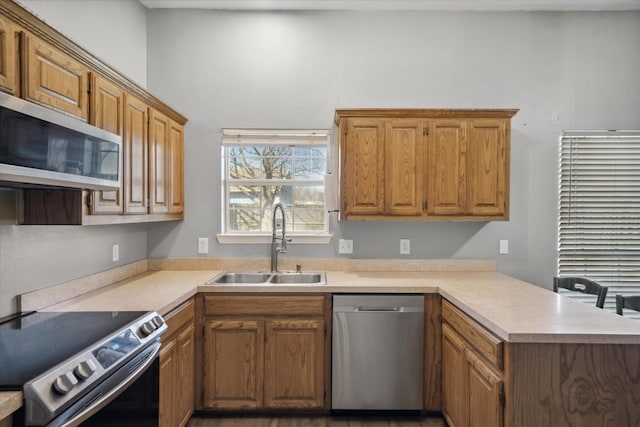 kitchen with light countertops, appliances with stainless steel finishes, brown cabinetry, a sink, and a peninsula