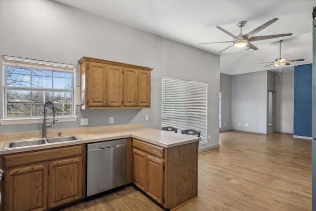 kitchen with light wood finished floors, light countertops, stainless steel dishwasher, a sink, and a peninsula