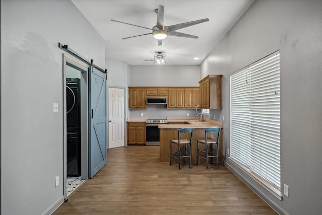 kitchen with electric range, a barn door, a sink, stacked washing maching and dryer, and a peninsula