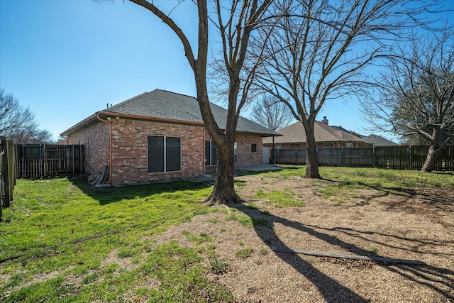 rear view of property featuring a patio, a fenced backyard, brick siding, a yard, and roof with shingles