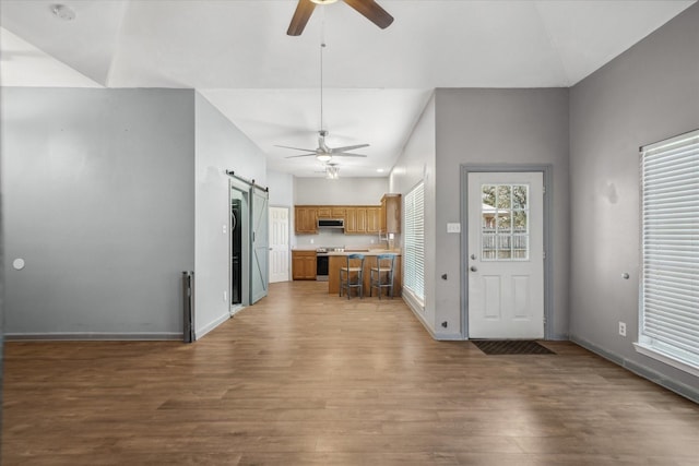 kitchen with a barn door, brown cabinetry, wood finished floors, stainless steel electric stove, and light countertops