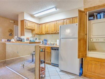 kitchen with a textured ceiling, stacked washer / dryer, light countertops, stainless steel dishwasher, and freestanding refrigerator