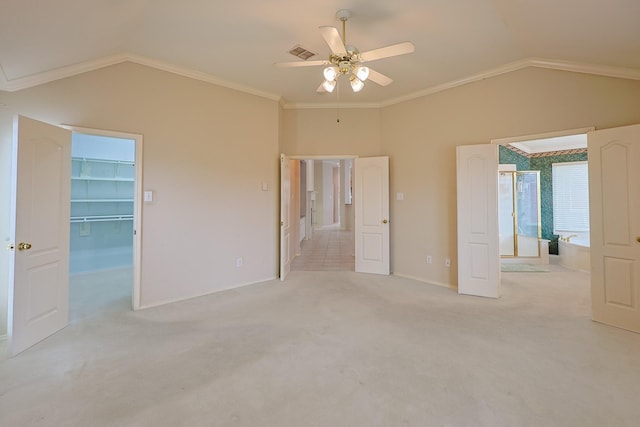 unfurnished bedroom featuring lofted ceiling, light carpet, visible vents, ornamental molding, and a walk in closet