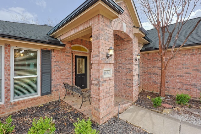 entrance to property featuring brick siding and a shingled roof