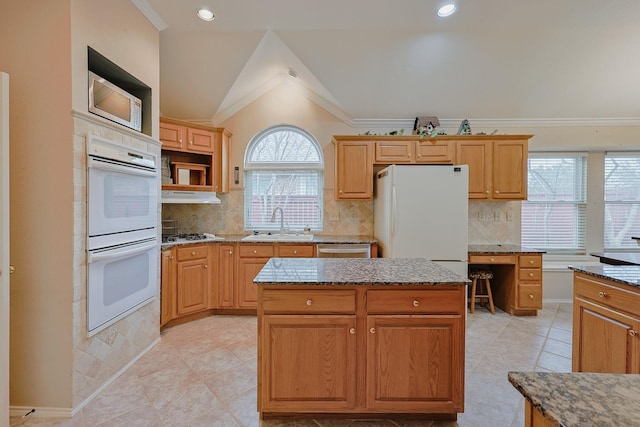 kitchen featuring lofted ceiling, white appliances, stone counters, and a sink