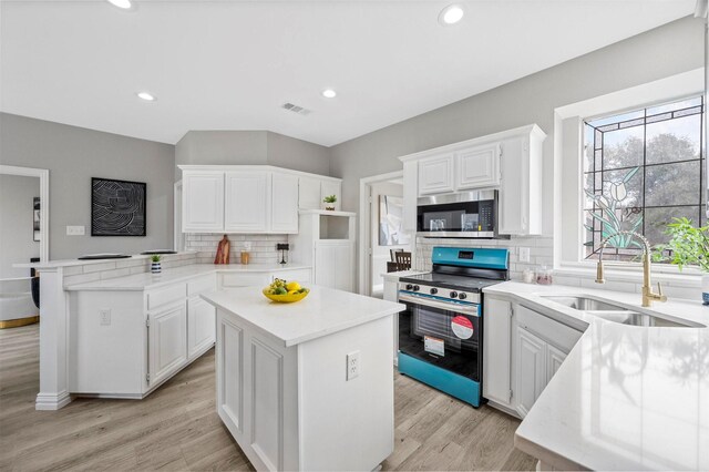 kitchen featuring visible vents, white cabinets, appliances with stainless steel finishes, a peninsula, and a sink