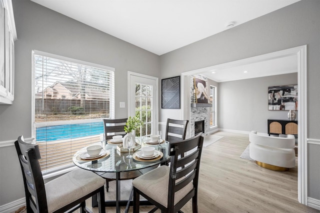 dining room with light wood-type flooring, a fireplace, and baseboards