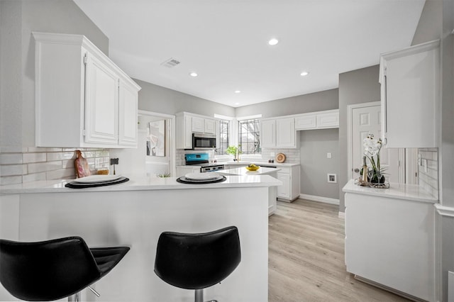 kitchen featuring visible vents, appliances with stainless steel finishes, white cabinetry, light wood-type flooring, and a peninsula