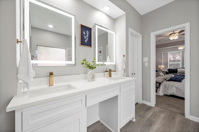 full bath with double vanity, ceiling fan, a sink, and wood finished floors