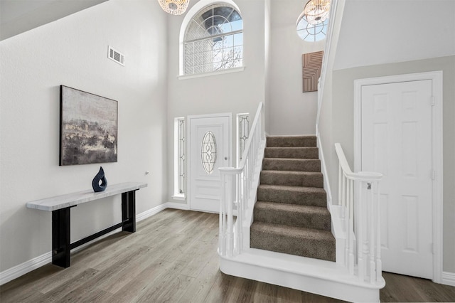 foyer entrance with a chandelier, stairway, wood finished floors, and visible vents