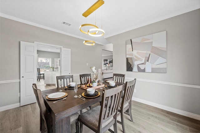 dining room featuring light wood-type flooring, visible vents, crown molding, and baseboards