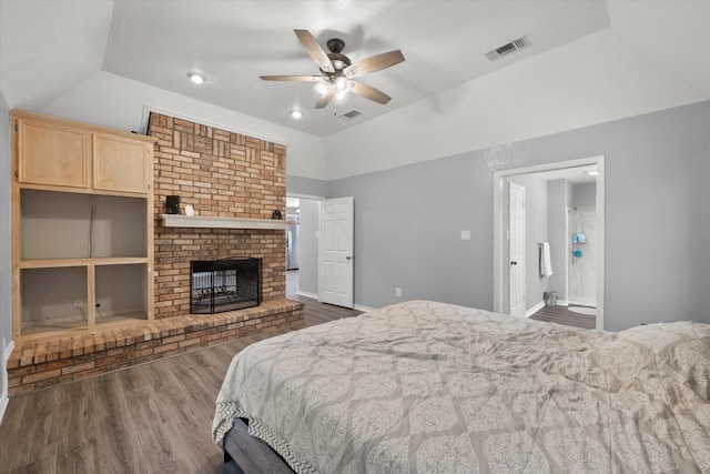 bedroom with lofted ceiling, a brick fireplace, visible vents, and dark wood finished floors