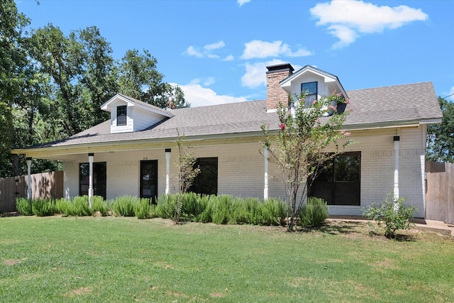 view of front facade featuring brick siding, a chimney, roof with shingles, fence, and a front yard