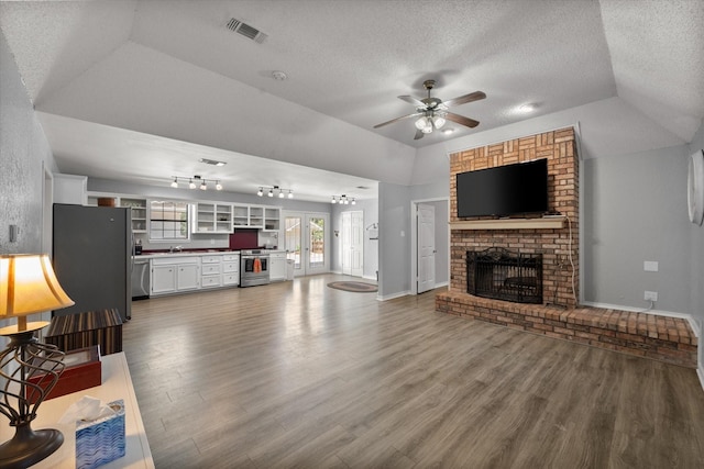 living area featuring a textured ceiling, a fireplace, wood finished floors, visible vents, and a ceiling fan