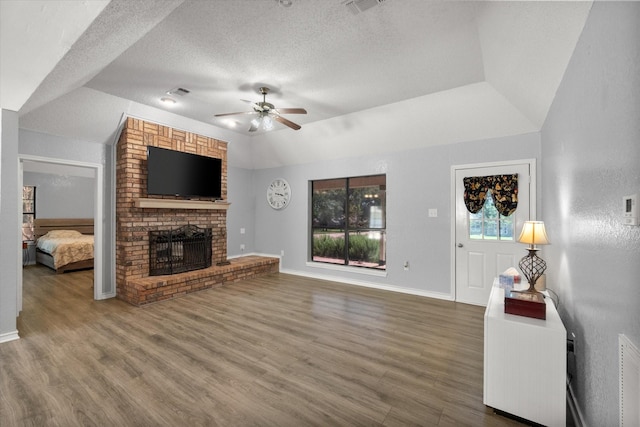 unfurnished living room with a brick fireplace, a textured ceiling, a ceiling fan, and wood finished floors