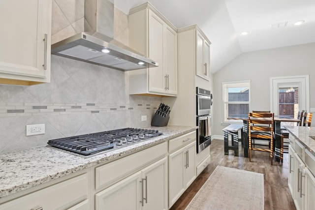 kitchen with lofted ceiling, wall chimney range hood, appliances with stainless steel finishes, and dark wood-type flooring