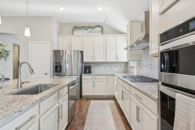 kitchen with dark wood-style flooring, a sink, wall chimney range hood, appliances with stainless steel finishes, and tasteful backsplash