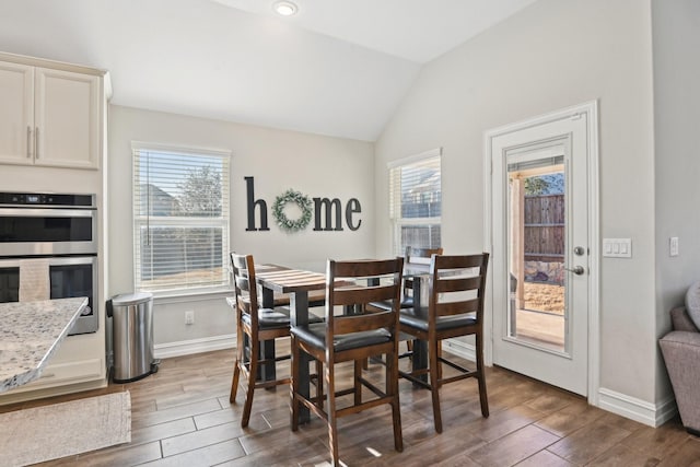 dining space featuring wood tiled floor, baseboards, and vaulted ceiling