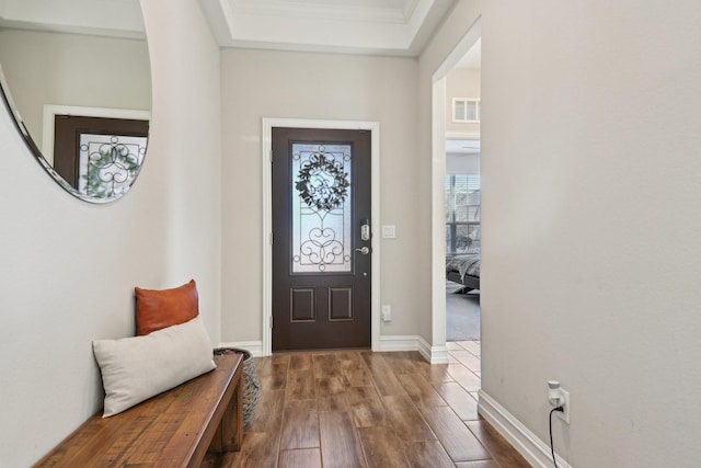 foyer entrance with baseboards, visible vents, dark wood finished floors, and crown molding