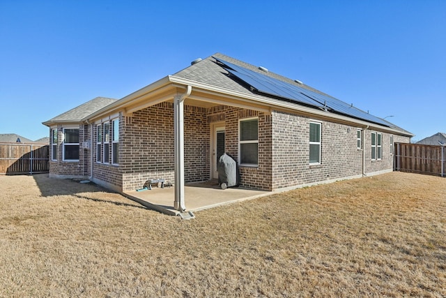 rear view of property with solar panels, brick siding, a patio area, and a fenced backyard