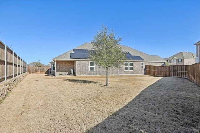 back of house with roof mounted solar panels, brick siding, and a fenced backyard